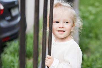 Adorable blomde baby girl is walking outdoors near the fence