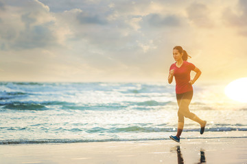 Woman running at the beach with sunset background.