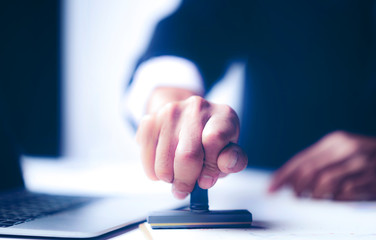 Close-up Of A Person's Hand Stamping With Approved Stamp On Document At Desk