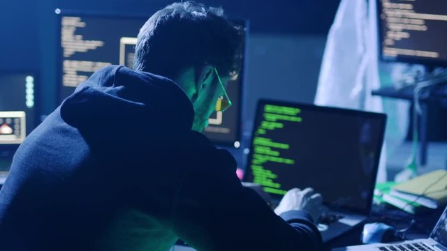 Skilled computer hacker typing code on laptop trying to steal critical information in the office at night.