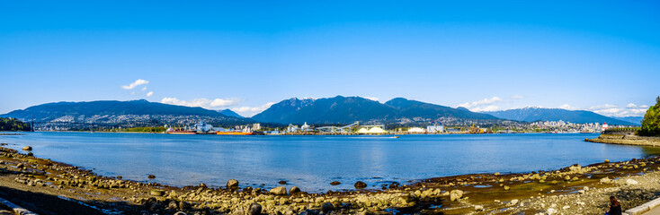 Fototapeta na wymiar Panorama View of the North Shore of the Vancouver Harbor with Grouse Mountain in the background. Viewed from the Stanley Park Seawall pathway