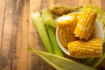 boiled corn cob in a plate with butter, on wooden textures and green stalks of corn, tasty homemade food, for a picnic, with space