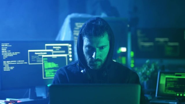 Portrait of menacing serious computer hacker working with codes on laptop at desk. Cyber crime and malware concept.