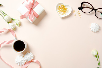 Flat lay home office desk. Female workspace with ribbon, coffee cup, gift box, marshmallows and roses on pink background. Top view feminine background with copy space for text.