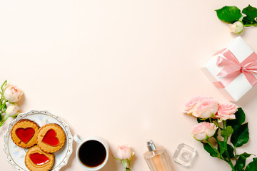 Frame made of biscuits, coffee cup, roses flowers bouquet, gift box. Flat lay women's desk table. Top view feminine background.