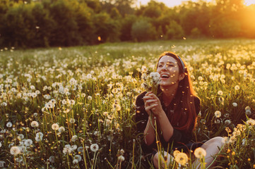 Beautiful Young Woman lying on the field in green grass and blowing dandelion. Outdoors. Enjoy...