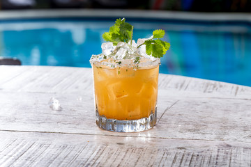 Yellow colored cocktail with ice and garnish on swimming pool setting
