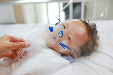 Toddler boy using nebulizer to cure asthma or pneumonia disease . Sick baby boy rest on patients...