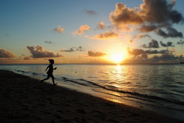 Silhouette of an unrecognizable girl running on the beach at sunset, with golden reflections in the water