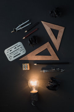 Creative idea for engineering, architecture or construction. Light bulb shining in black on black flat lay with crumpled paper balls, rulers, pencils