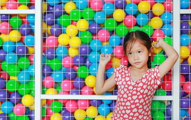 Fototapeta na wymiar Peaceful little Asian girl catching cage of playground colorful toy ball with looking out.