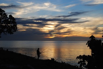Silhouette of an unrecognizable fisherman with his fishing pole at sunset 