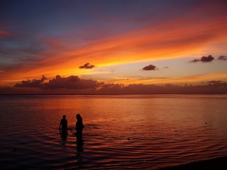 Breathtaking sunset in the beach with two unrecognizable people standing in the water 