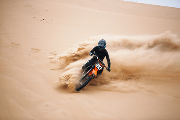 Motorcyclist on a cross-country motorcycle go fast at the desert. Biker make a turn on a dune at...
