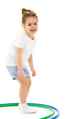A little girl in a white T-shirt performs exercises with a hoop.