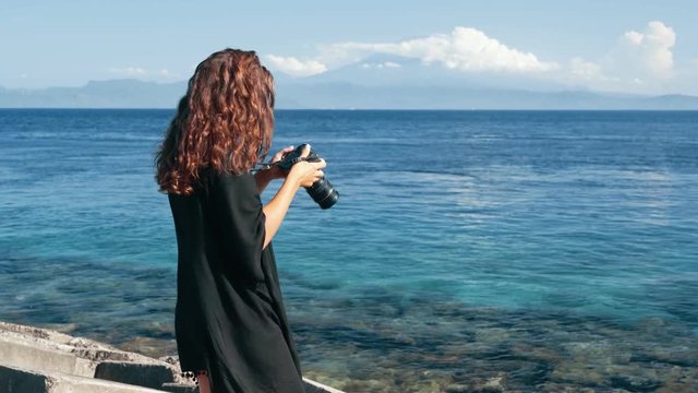 Side view of girl photographer takes pictures of ocean and mountains.