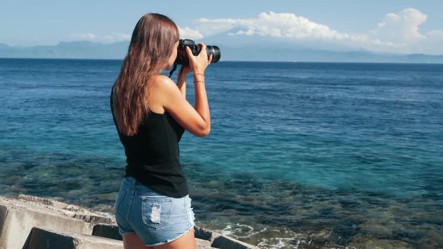 Side view of girl tourist photographer takes pictures of ocean and mountains.