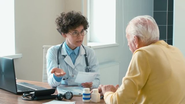 Female doctor sitting in her room with old patient and explaining her appointment in detail