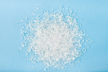 Top view of pile of broken white small glass pieces on blue background. Sharp glass fragments ready to be remelted.