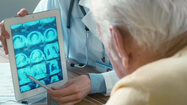 Doctor and adult patient examining MRI images on tablet computer, pointing fingers