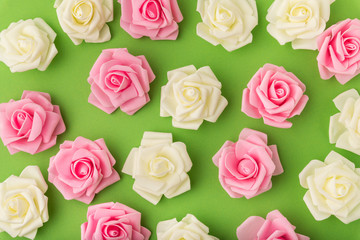 Top view of pink and yellow artificial flowers on a green background. Artificial rosebuds for decoration.