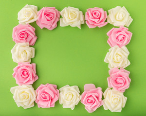 Fototapeta na wymiar Rectangular frame made up of pink and yellow artificial flowers on green background. Border of artificial rosebuds for decoration. Template for a festive, greeting, joyful, wedding card.