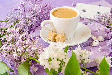 Coffee with  and cane sugar on a lilac table, surrounded by lilac flowers. Old music cassettes and headphones.