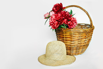 Straw hat with a bouquet of luxurious, lush coral and pink peonies. Flowers in a wicker basket on a white background.