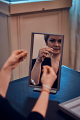 Elegant woman is trying on new jewel necklace in front of the mirror.