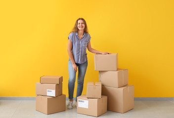 Young woman with many cardboard boxes near color wall