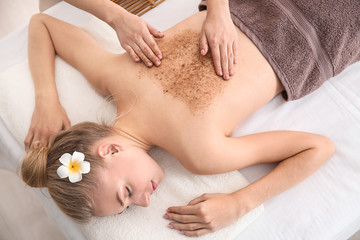 Fototapeta na wymiar Young woman undergoing treatment with body scrub in spa salon