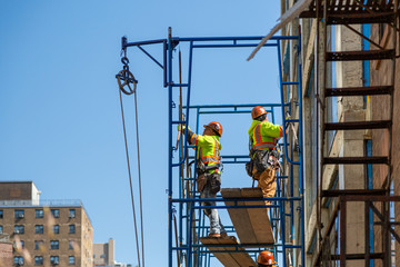 Construction workers at work on a skyscraper building renovation and construction site on a scaffold