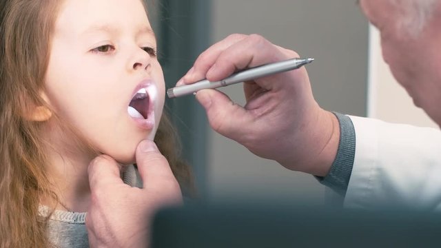 Close up shot of doctor watching little patient's throat with penlight and making diagnosis