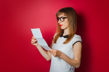 A young woman with a smile is reading a letter on a dark pink background. Concept notice, good...