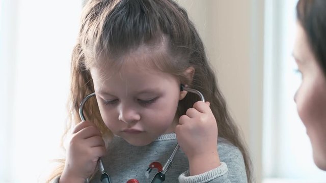 Little girl sitting near mother and trying to put phonendoscope on