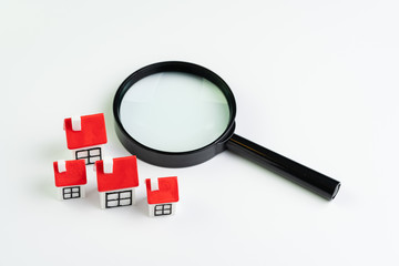 Search for house and home loan, real estate or mortgage loan concept, magnifying glass with group of small cute miniature houses with red roof on white background