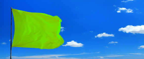 Conceptual image of waving blank green flag over sunny blue sky