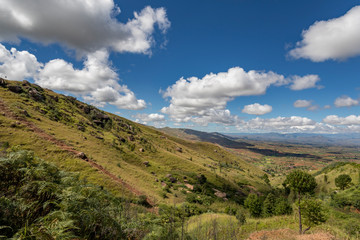 Fototapeta na wymiar Rural mountain landscape in Central Madagascar. Deforestation hills, a valley and mountains on the background with clouds above