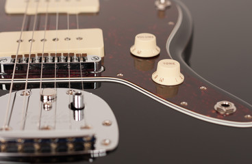 Close up of control tone  on  black electric guitar, studio shoot. Red tortoise shell pickguard, alder body, two single coil.