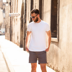 Naklejka na ściany i meble Hipster handsome male model with beard wearing white blank t-shirt with space for your logo or design in casual urban style