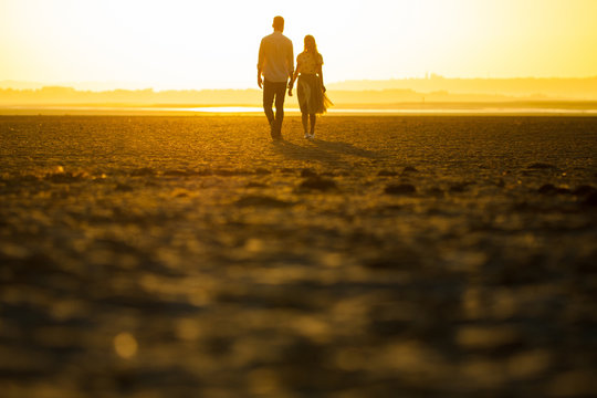 Couple on the beach walking hand in hand during sunset