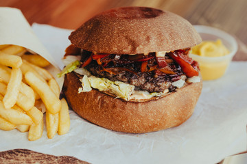 Delicious fresh homemade cheese burger with meat, cheese, tomatoes, lettuce and onion rings in Kraft paper and french fries . street food on wooden table  on wooden background