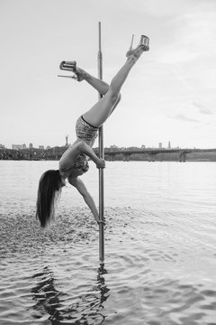 Monochrome portrait of athletic beautiful redhead woman with long hair on the pole in river Dnieper on cityscape background in the evening (sunset)