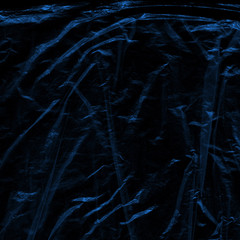 Transparent blue plastic wrap on the black background. Plastic shopping bag texture. Reusable trash and waste.