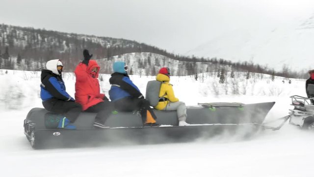 tourists in colorful jackets sit and ride snow banana boat