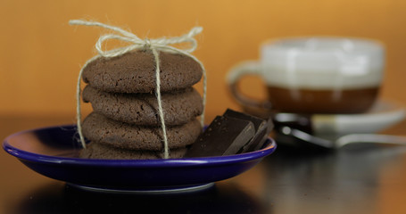Tasty looking chocolate cookie on a blue plate on dark surface. Warm background