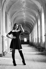 Young beautiful short hair blonde woman in black climbing the stairs, black and white photo. Side view of elegant romantic mysterious lady with movie star look in interior with bricks walls