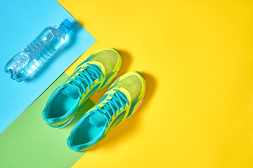 Pair of sport running shoes and water on colorful background. New sneakers on green and yellow pastel background, copy space. Overhead shot. Top view, flat lay