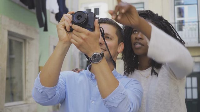 Happy couple with digital photo camera. Smiling African American woman with dreadlocks and Caucasian man taking photos with modern camera. Photography concept