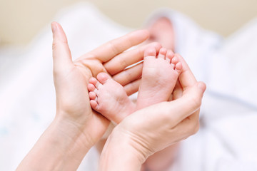 Obraz na płótnie Canvas Mother holding newborn baby feet in hands. Mom taking care about infant child after taking bath. Parents childcare. Children healthcare and happy family